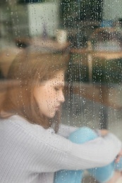 Photo of Depressed young woman near window, view from outside