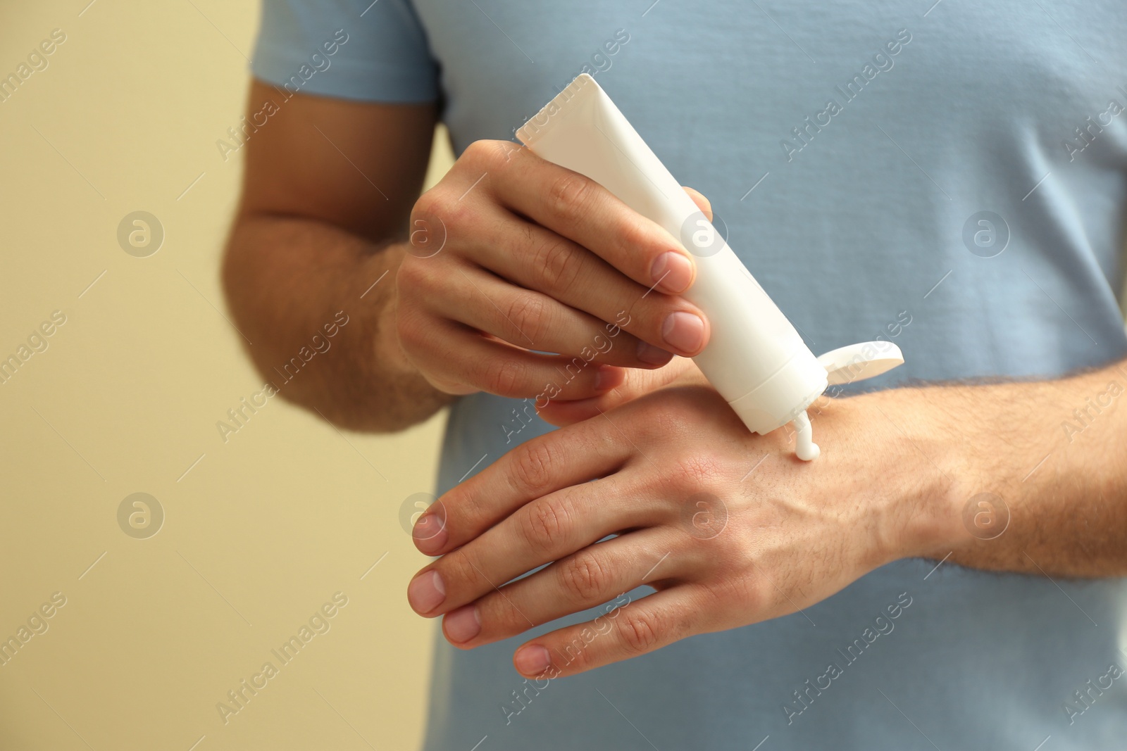 Photo of Man applying cream from tube onto hand on yellow background, closeup