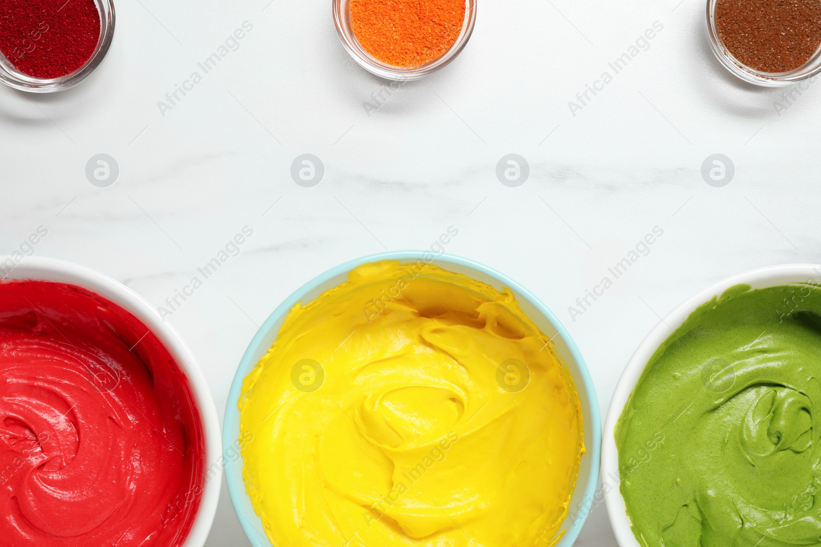 Photo of Bowls of different cream with food coloring on white marble table, flat lay