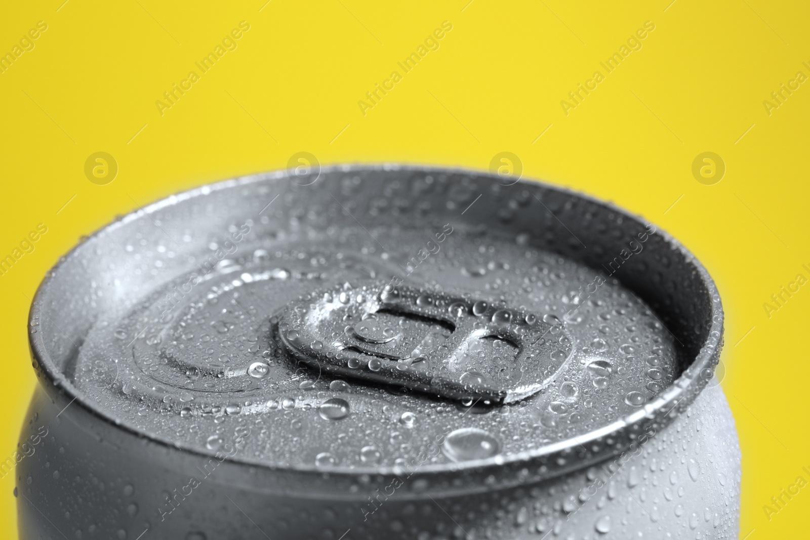 Photo of Aluminum can of beverage covered with water drops on yellow background, closeup