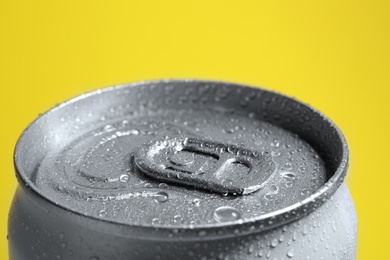 Aluminum can of beverage covered with water drops on yellow background, closeup