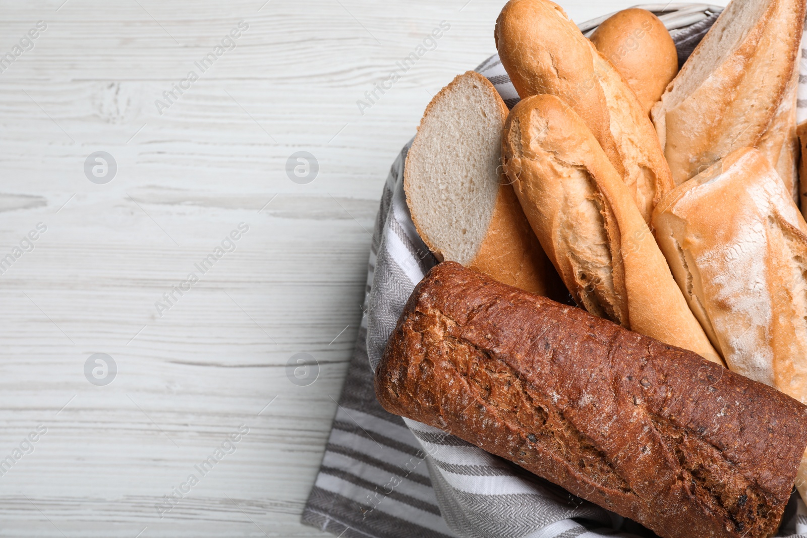 Photo of Different tasty baguettes in basket on white wooden table, top view. Space for text