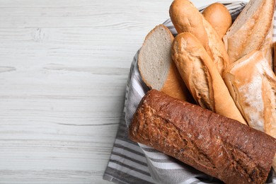 Different tasty baguettes in basket on white wooden table, top view. Space for text