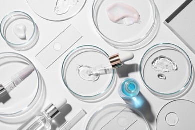 Flat lay composition with petri dishes and samples of cosmetic serums on white background