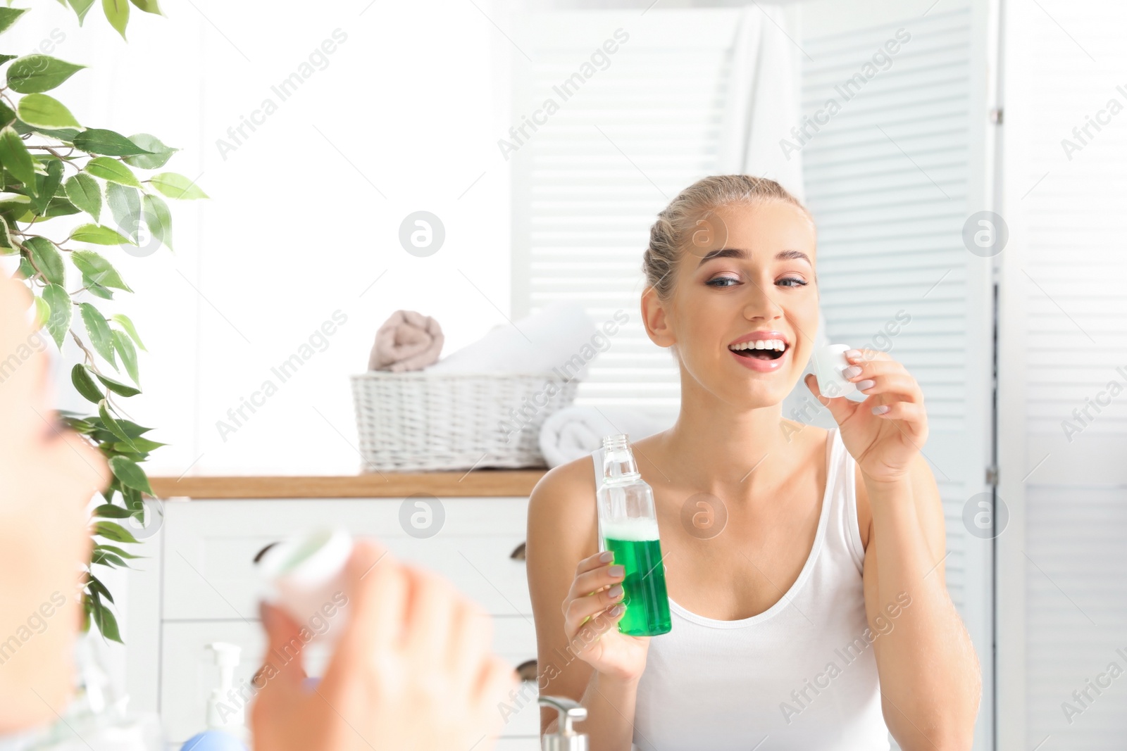 Photo of Woman holding bottle and cap with mouthwash in bathroom. Teeth care