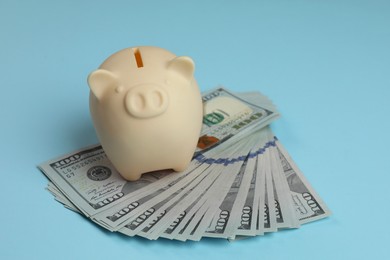 Photo of Money exchange. Dollar banknotes and piggy bank on light blue background, closeup