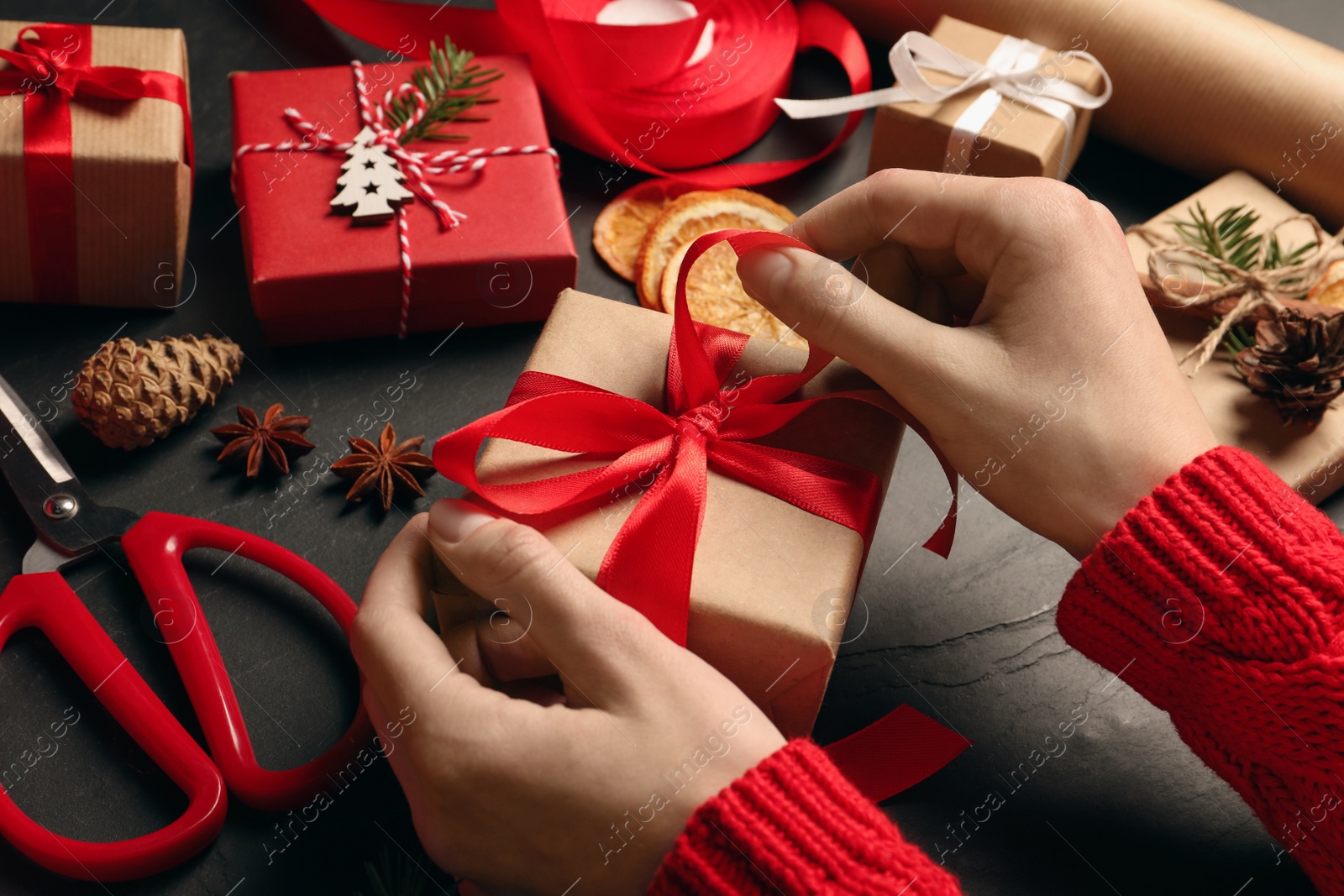 Photo of Woman decorating gift box at black table, closeup. Christmas present
