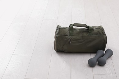 Sports bag and dumbbells on white floor, space for text