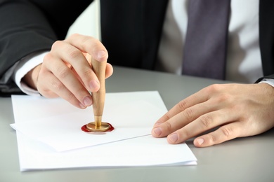 Male notary sealing document at table, closeup