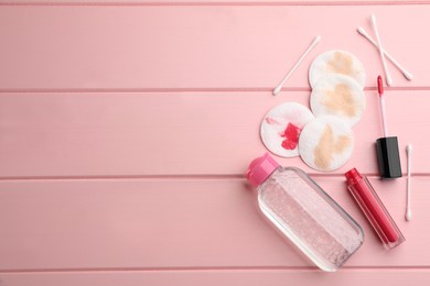 Photo of Dirty cotton pads, swabs, lipstick and micellar cleansing water on pink wooden background, flat lay. Space for text