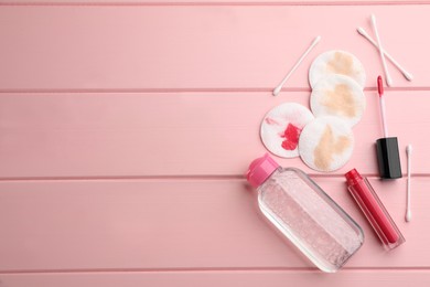 Dirty cotton pads, swabs, lipstick and micellar cleansing water on pink wooden background, flat lay. Space for text