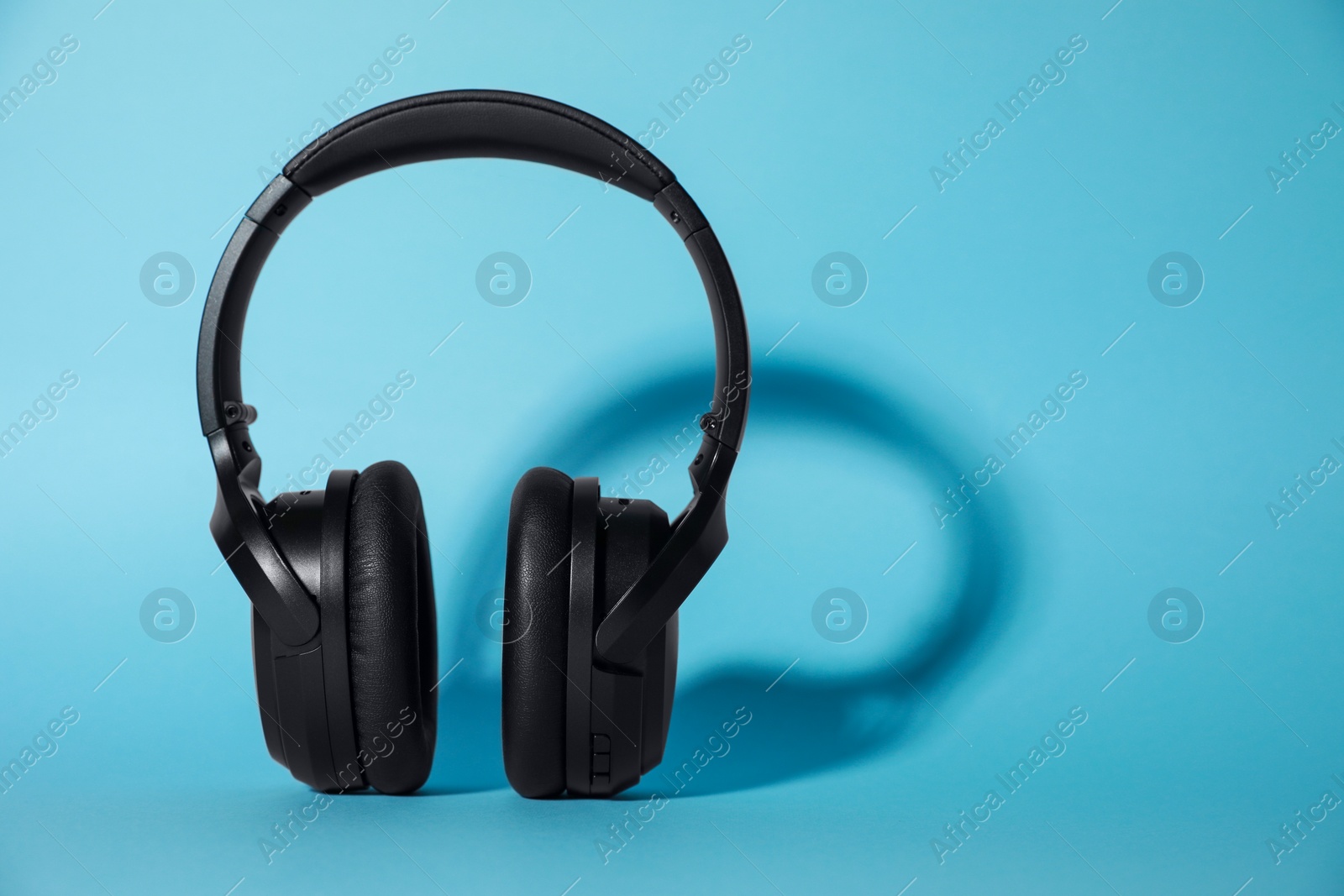 Photo of Modern wireless headphones on light blue background. Space for text