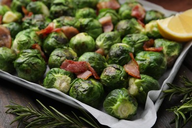 Photo of Delicious roasted Brussels sprouts, bacon and rosemary on wooden table, closeup