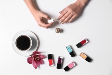 Photo of Woman applying nail polish near coffee and bottles on white background, top view