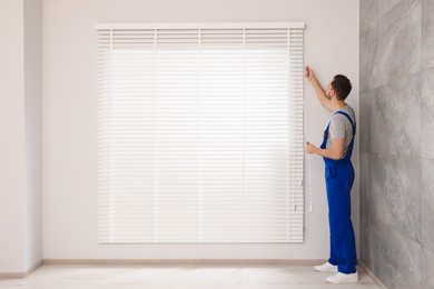 Worker in uniform opening or closing horizontal window blind indoors
