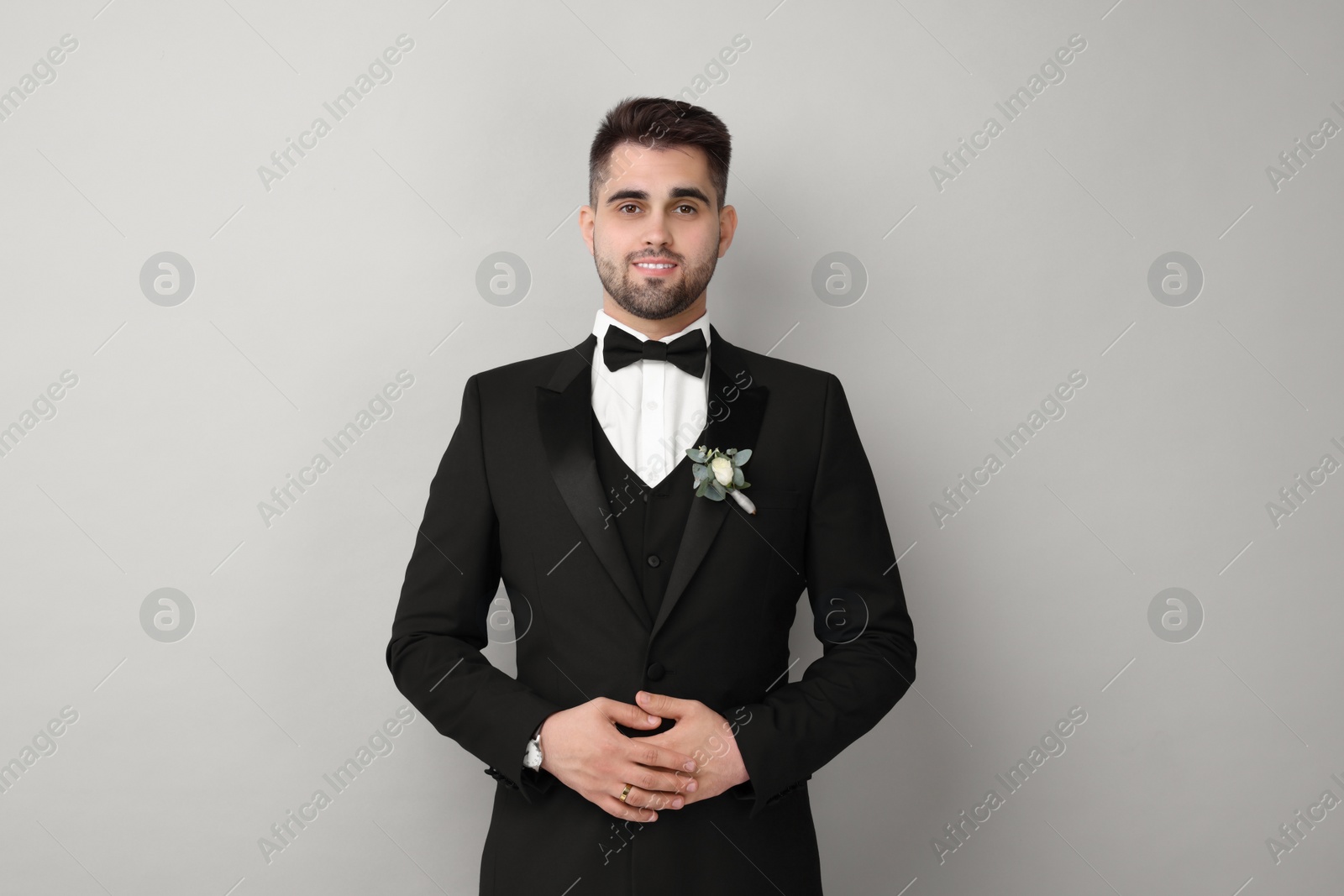 Photo of Handsome young groom with boutonniere on light grey background. Wedding accessory