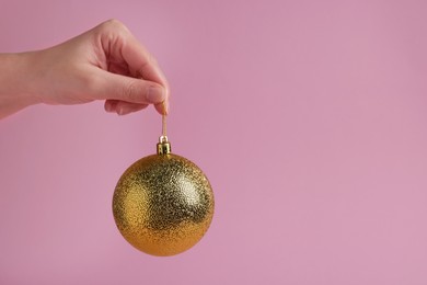 Photo of Woman holding golden Christmas ball on pink background, closeup. Space for text