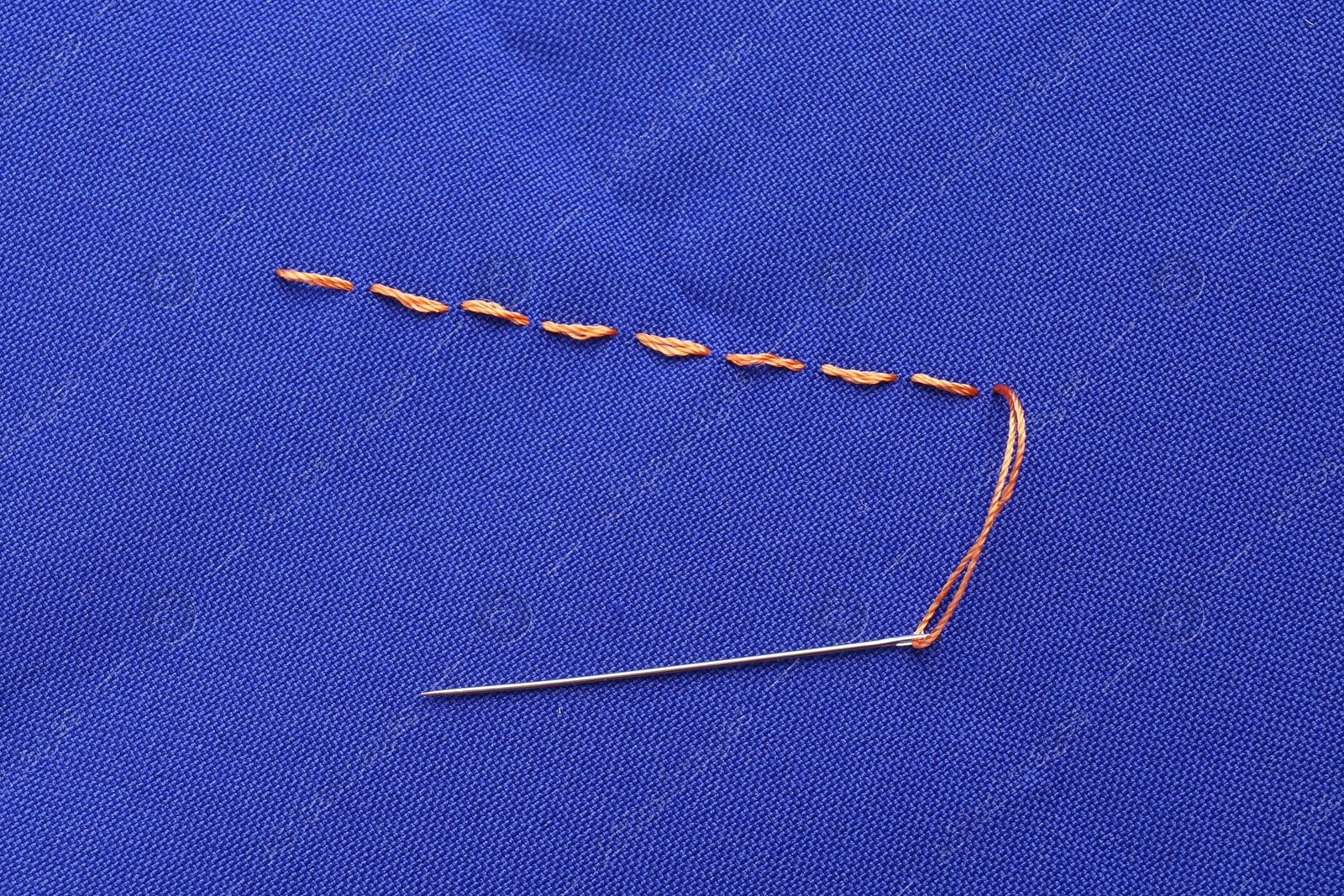 Photo of Sewing needle with thread and stitches on blue cloth, top view