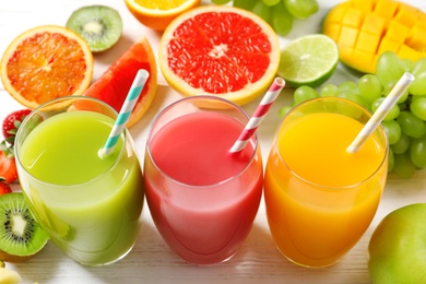 Glasses of different juices with straws and fresh fruits on wooden table, view from above