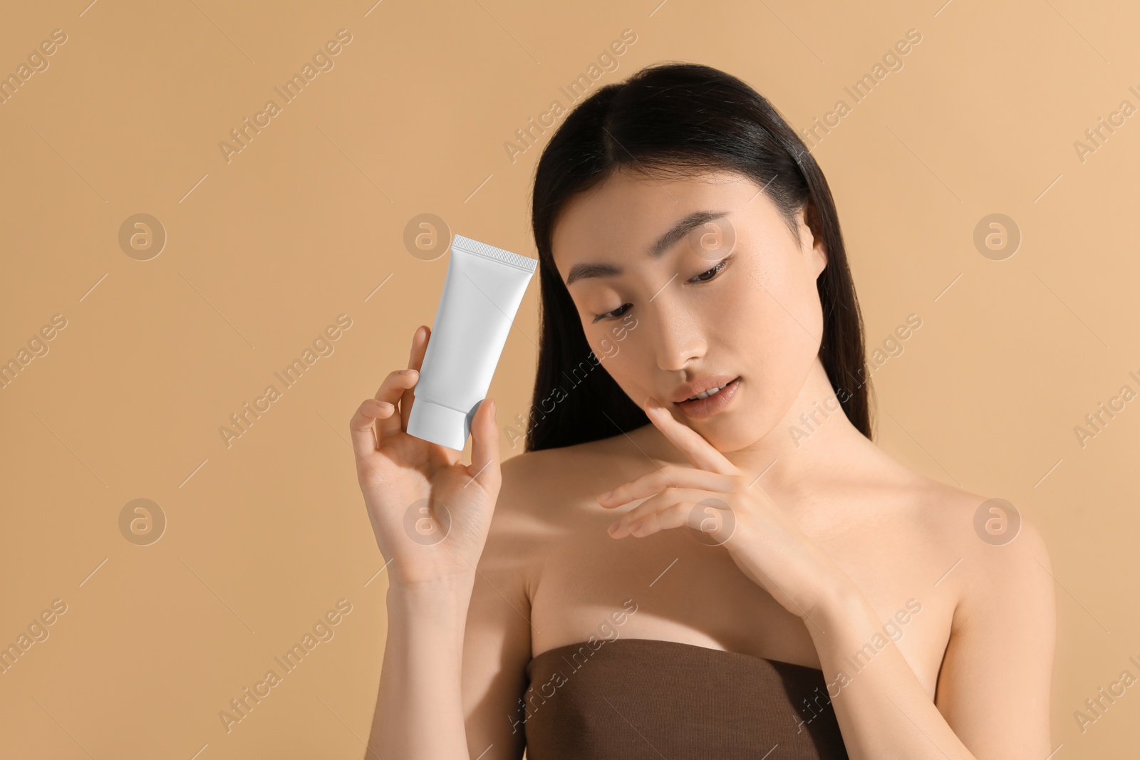 Photo of Beautiful young woman holding sun protection cream on beige background, space for text