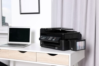 Modern printer with paper near laptop on white desk at home