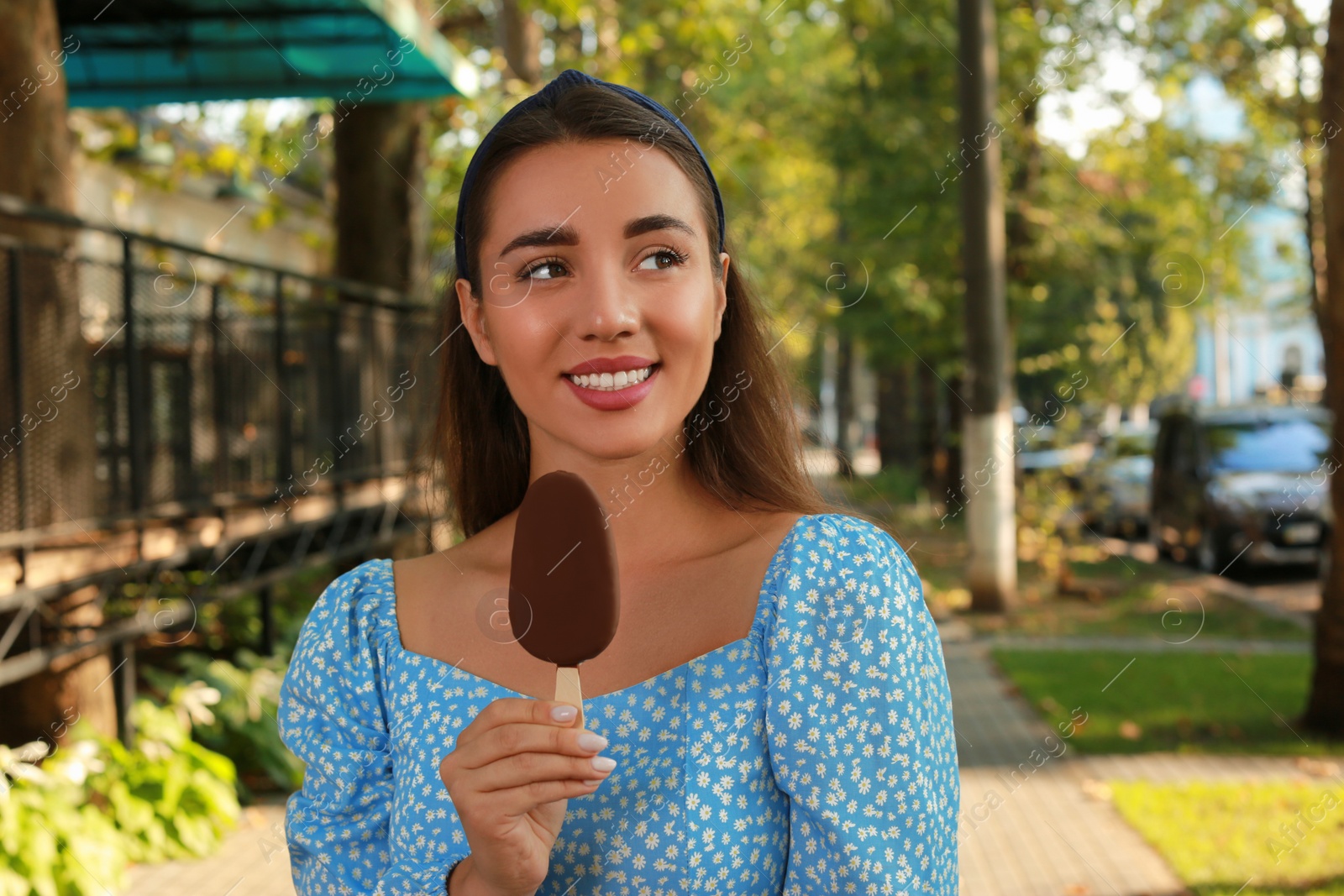 Photo of Beautiful young woman holding ice cream glazed in chocolate on city street