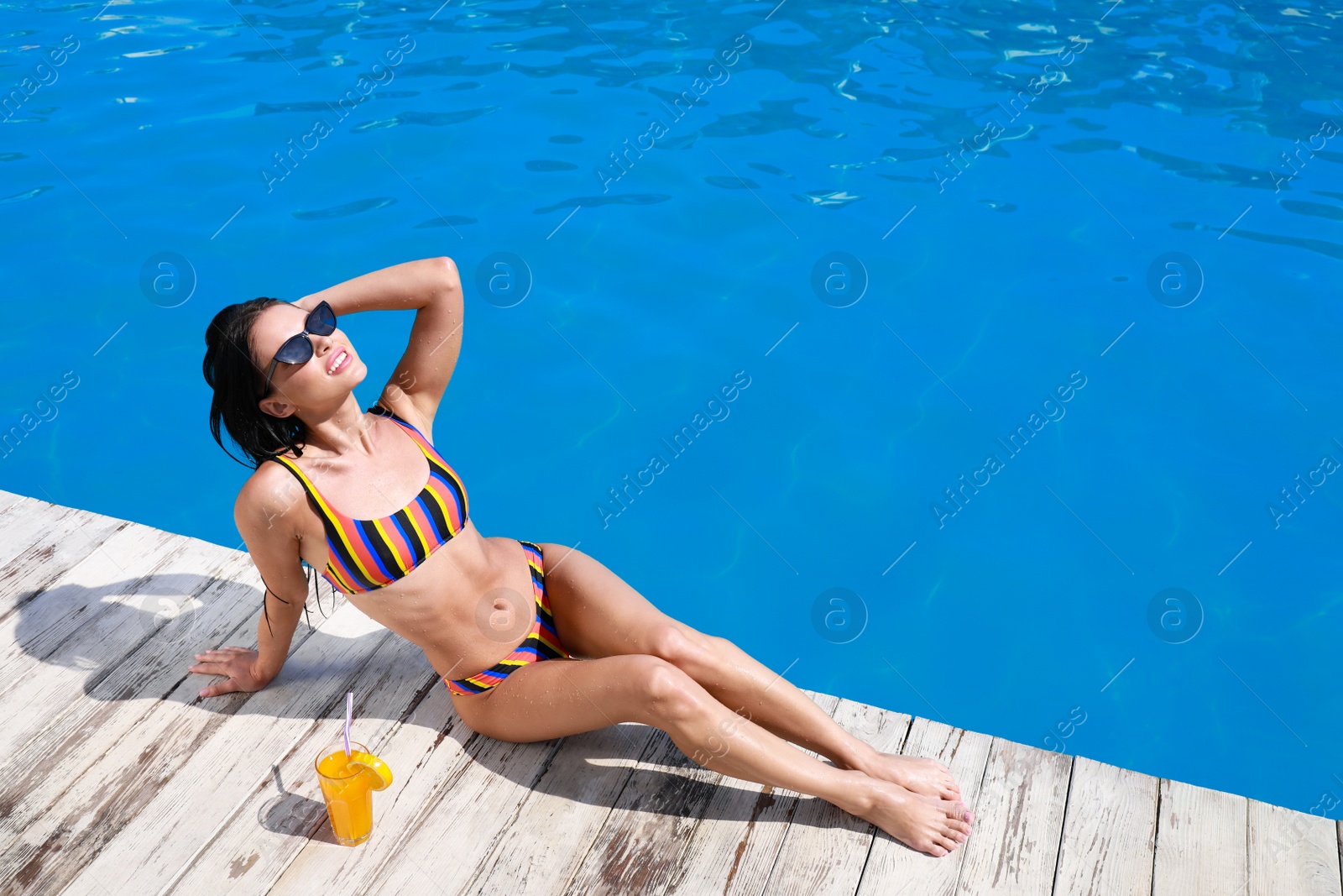 Photo of Beautiful young woman in bikini with refreshing cocktail near swimming pool on sunny day. Space for text