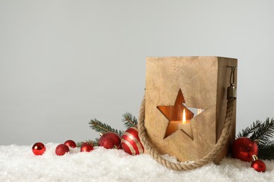 Composition with wooden Christmas lantern on snow against light grey background, space for text