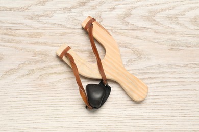 Slingshot with pebble on wooden background, top view