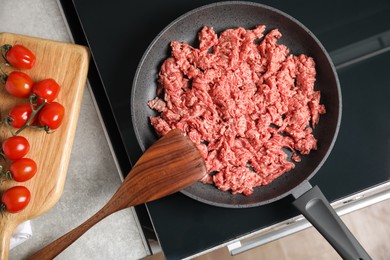 Photo of Frying pan with raw minced meat on induction stove indoors, flat lay