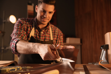 Photo of Man cutting leather with scissors in workshop