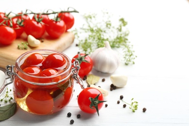 Photo of Glass jar of pickled cherry tomatoes and ingredients on white wooden table. Space for text