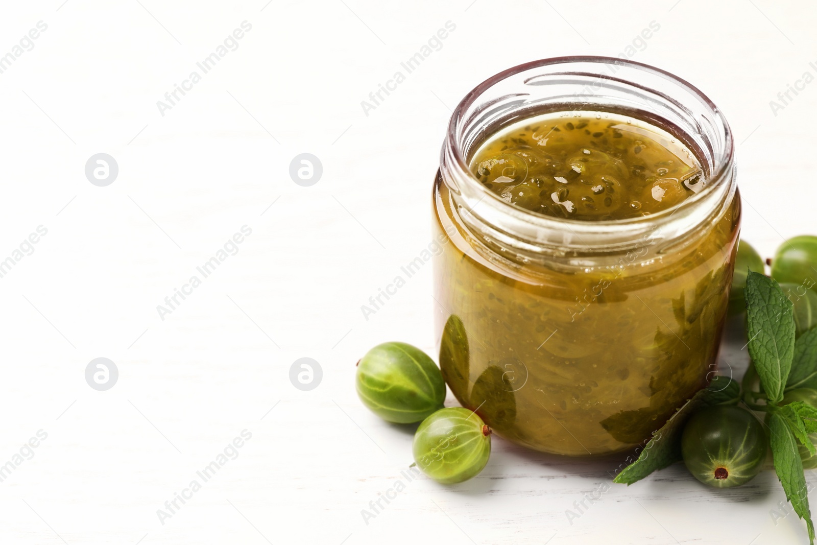 Photo of Jar of delicious gooseberry jam and fresh berries on white wooden table, closeup. Space for text