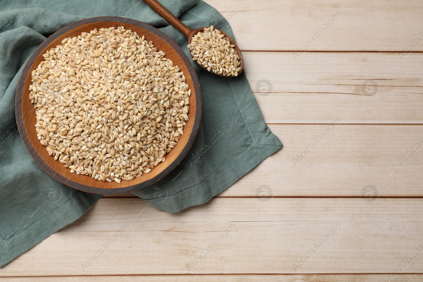 Photo of Dry pearl barley in bowl and spoon on light wooden table, top view. Space for text