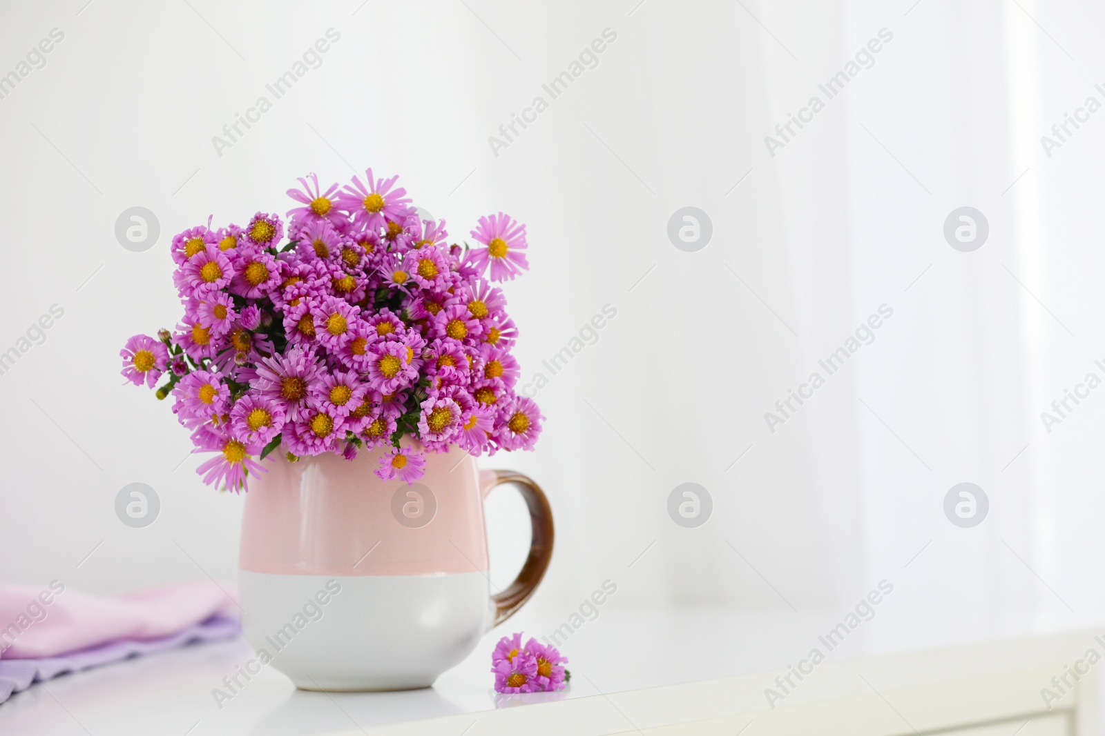 Photo of Cup with beautiful flowers on white table in light room. Space for text