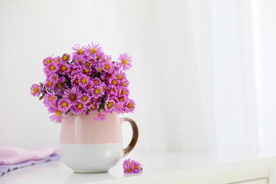 Cup with beautiful flowers on white table in light room. Space for text