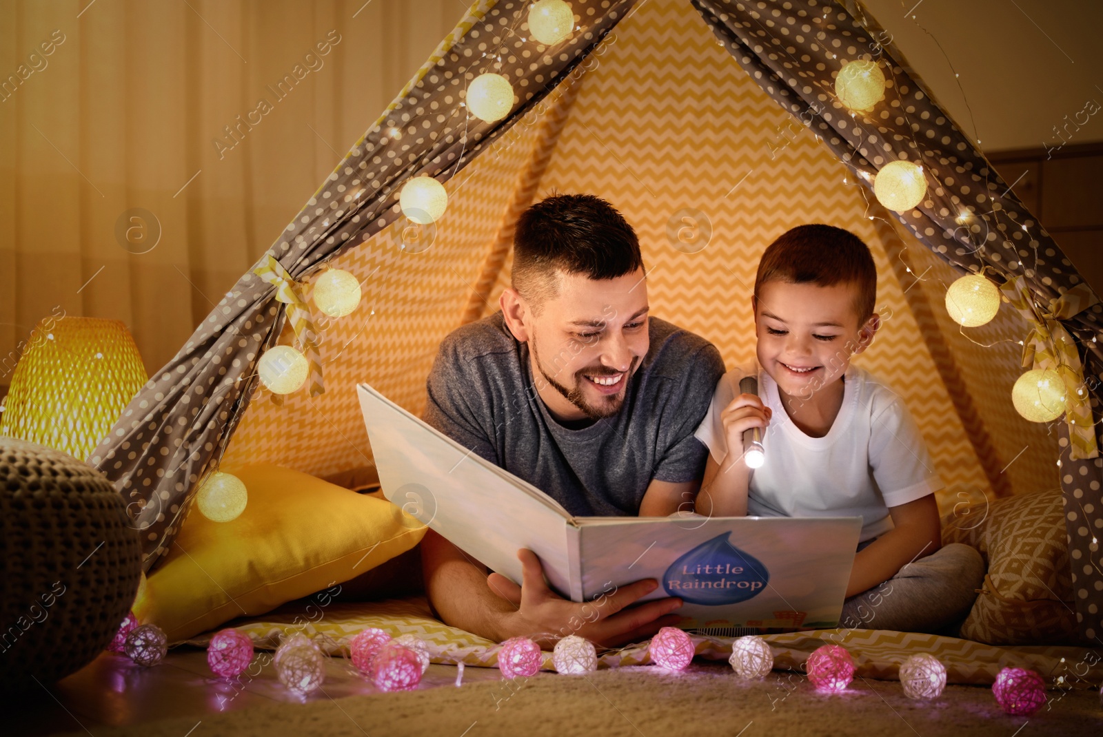 Photo of Father and son with flashlight reading book in play tent