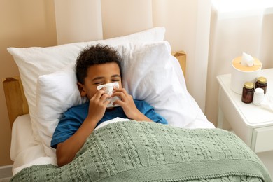 African-American boy with scarf and tissue blowing nose in bed indoors, above view. Cold symptoms