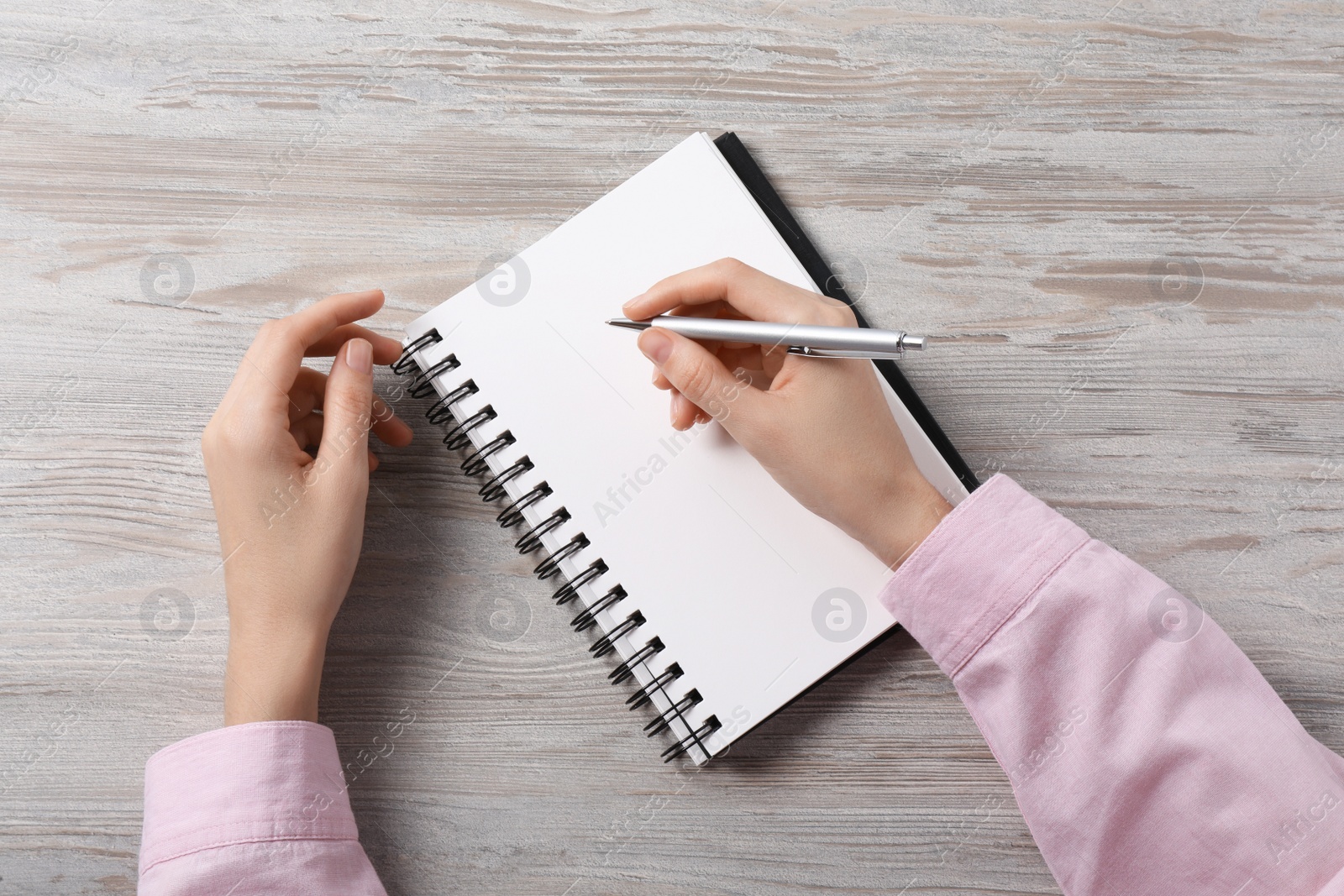 Photo of Woman writing in notebook at white wooden table, top view