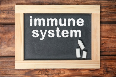 Image of Small blackboard with text Immune System and chalk on wooden background, top view