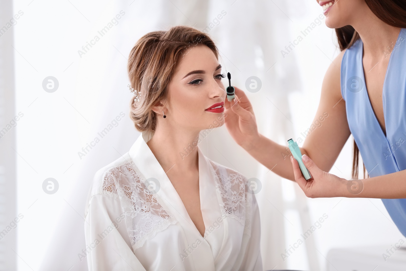 Photo of Makeup artist preparing bride before her wedding in room