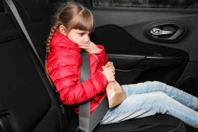 Little girl with paper bag suffering from nausea in car