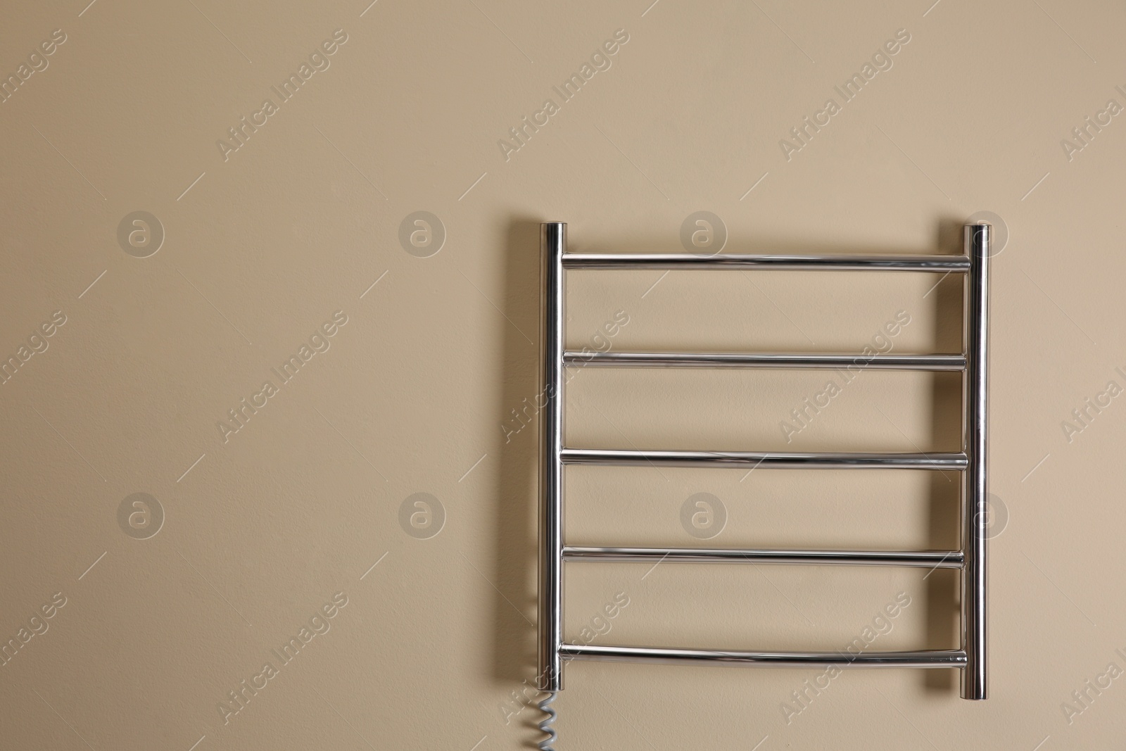 Photo of Modern heated towel rail on beige wall. Space for text