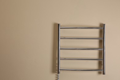 Photo of Modern heated towel rail on beige wall. Space for text