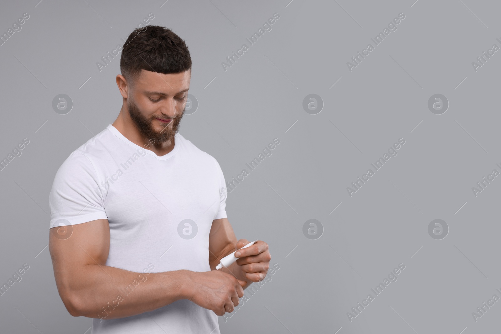 Photo of Handsome man applying body cream on light grey background, space for text