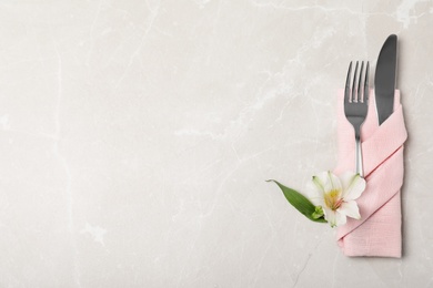 Folded napkin with fork, knife and flower on table, top view. Space for text