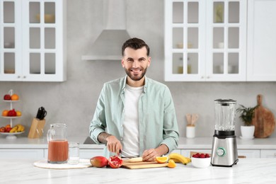 Photo of Handsome man preparing ingredients for tasty smoothie at white marble table in kitchen
