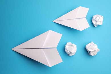 Photo of Handmade white planes and crumpled pieces of paper on light blue background, flat lay