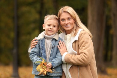 Photo of Portrait of happy mother and her son with dry leaves in autumn park