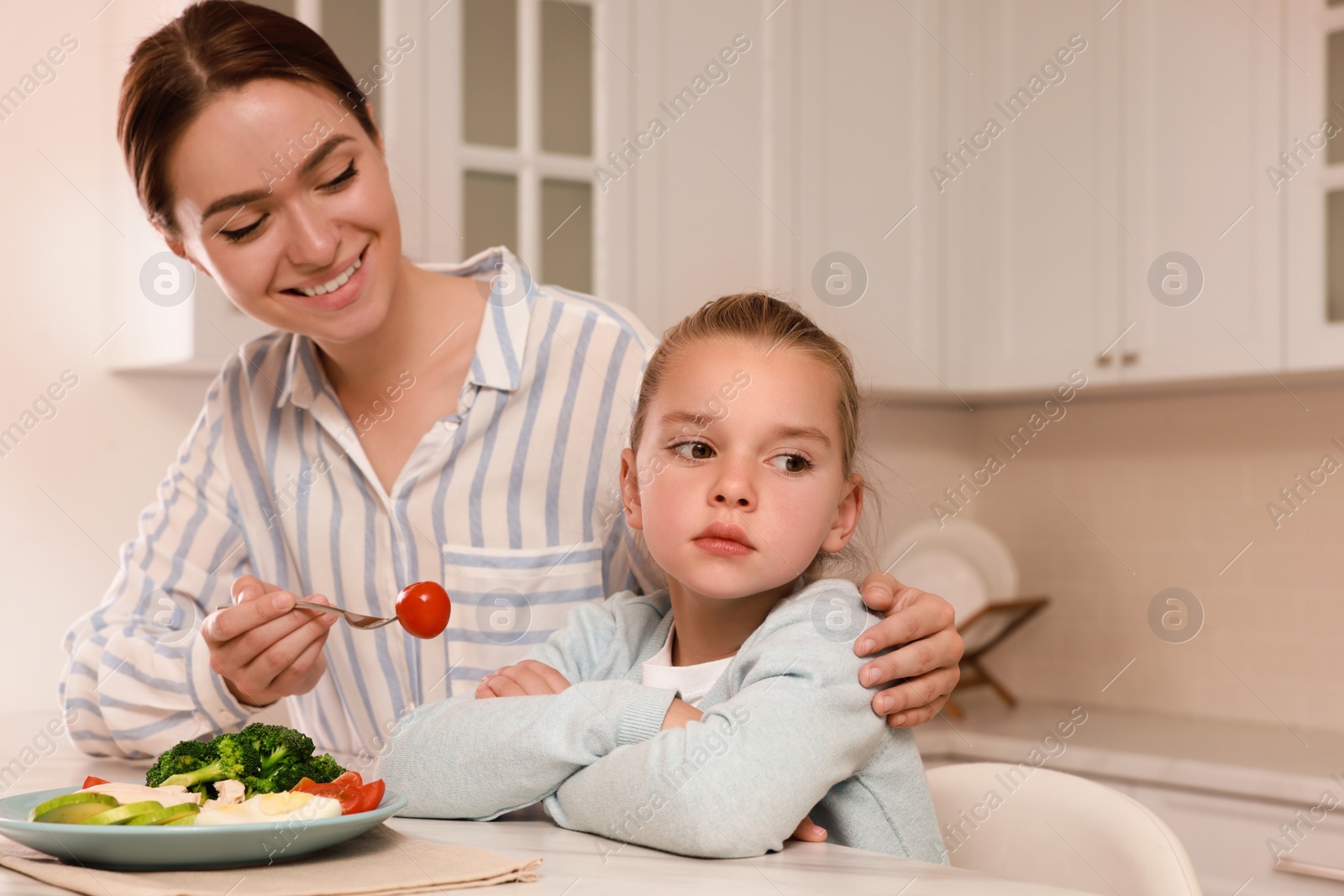 Photo of Mother feeding her daughter in kitchen. Little girl refusing to eat dinner